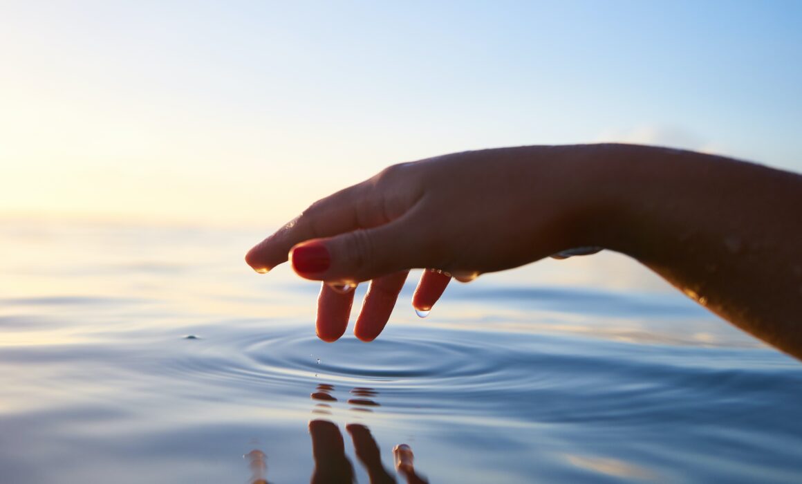 hand creating ripples in a reflective body of water